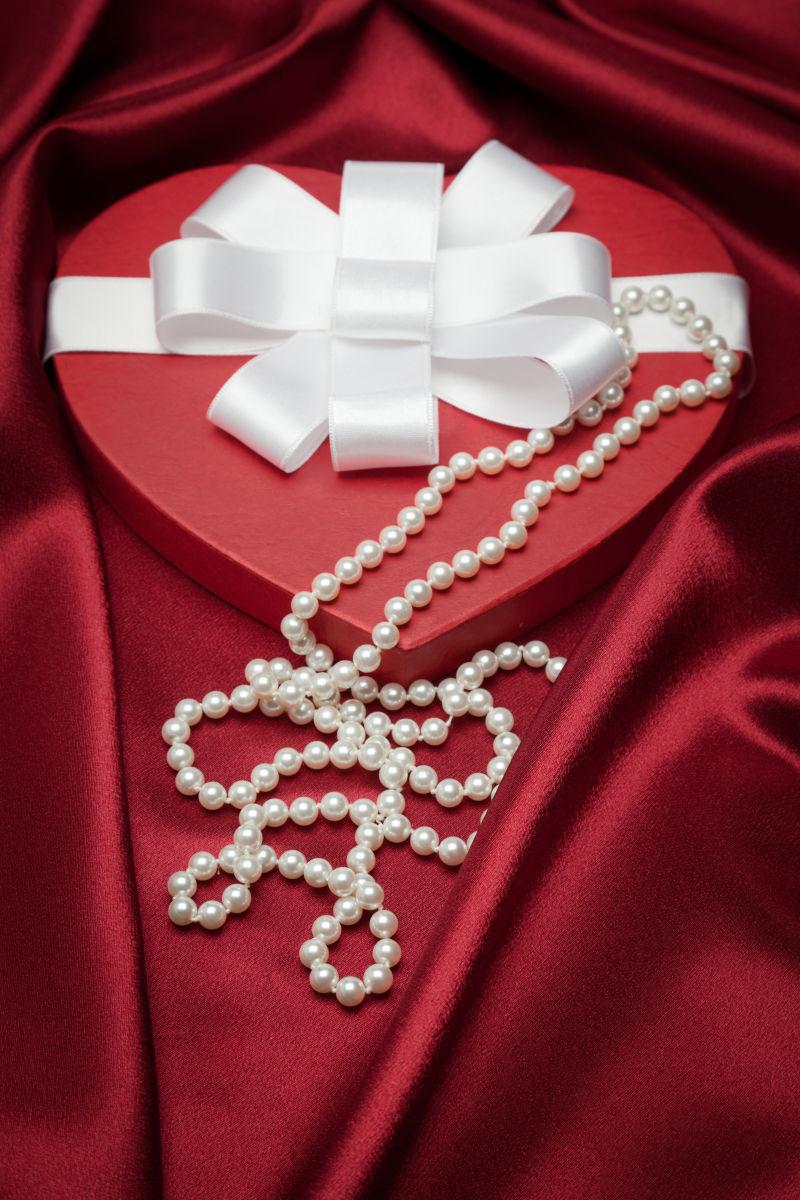 红色缎子背景下的白色缎子蝴蝶结心形礼盒