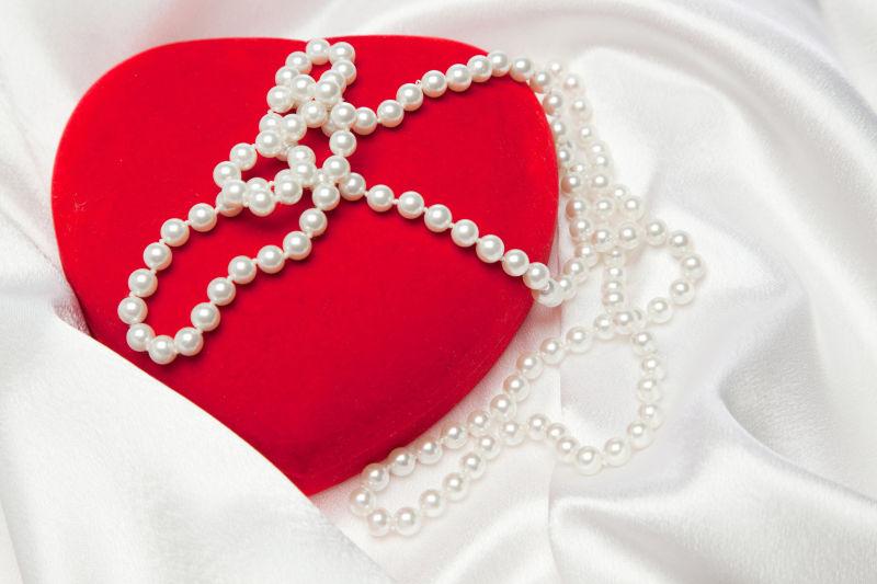白色缎纹背景下的红色心形首饰盒上的珍珠饰品