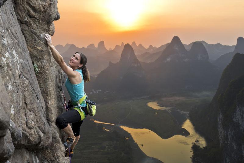 日落下攀登岩石的女登山者