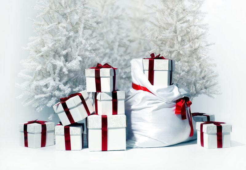 白色背景下落满雪的圣诞树旁的白色和红色的礼品盒