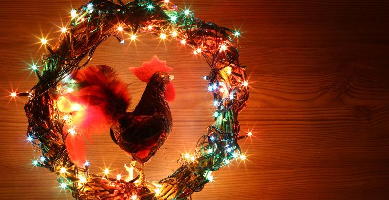 暖色木板背景下的圣诞节彩灯花环后的公鸡