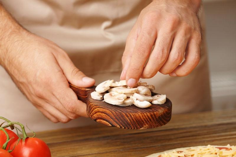 男性手在木桌上准备蘑菇比萨