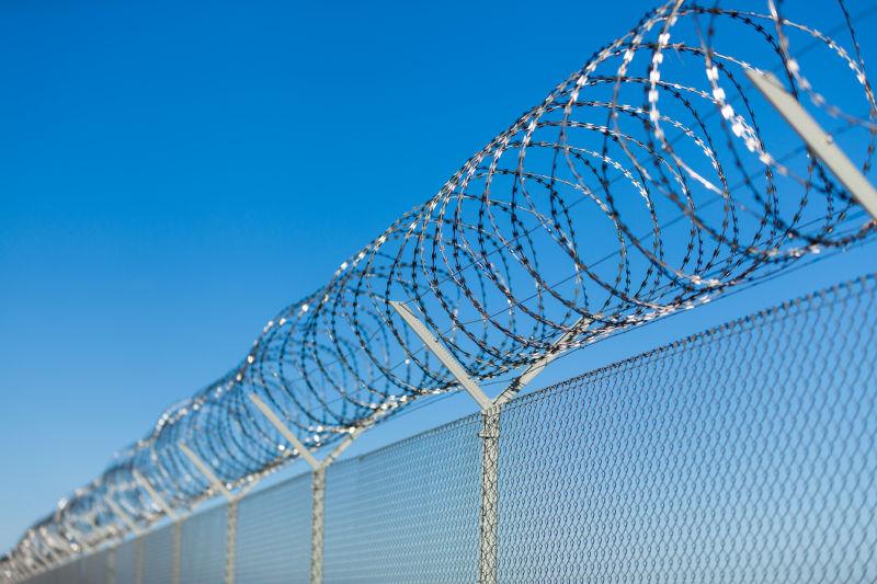 蓝天背景下监狱栅栏上的钢刺