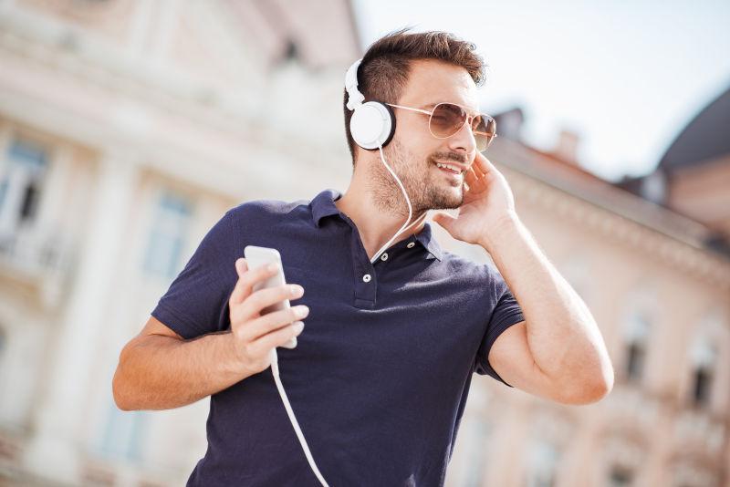 在户外拿着手机戴耳机听音乐的男人