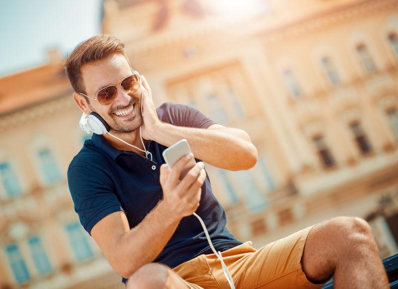 在户外听音乐玩手机微笑的男人