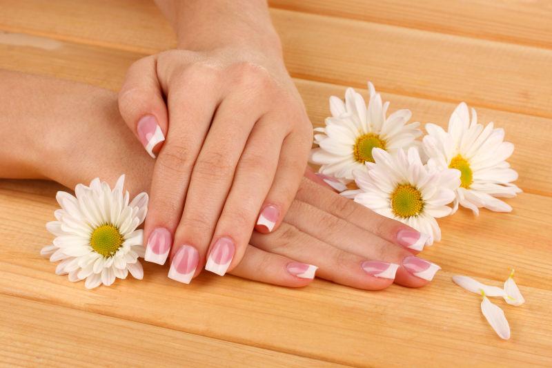 木制地板上女子双手的指甲和白色的花