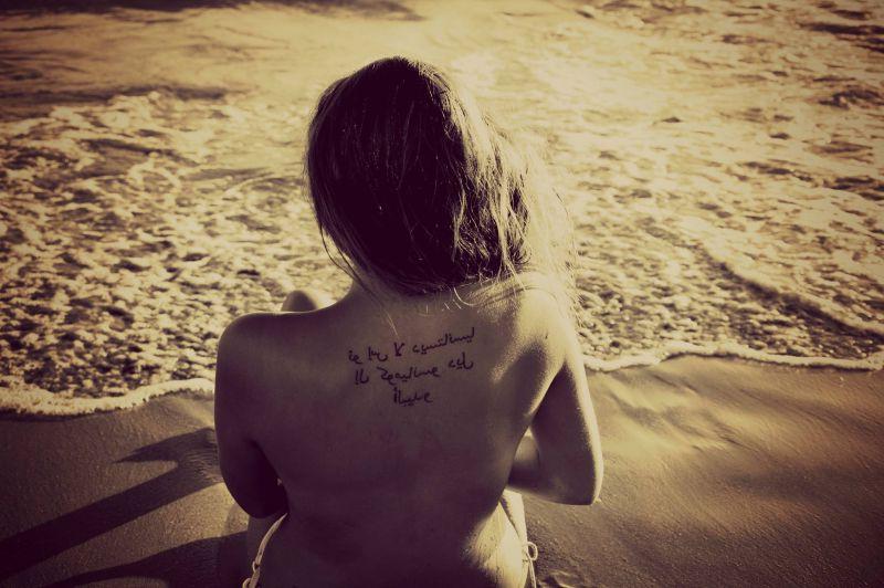 金色沙滩上后背有纹身的坐着的美女背影