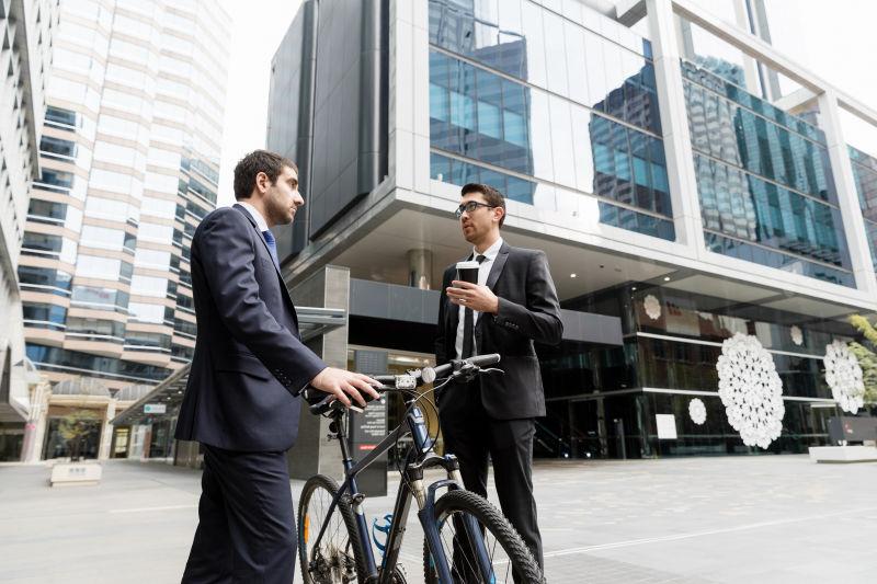 城市建筑背景下推着自行车交谈的两个年轻的商人