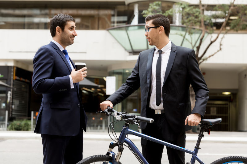 城市建筑背景下两位在市中心推着自行车的年轻商人