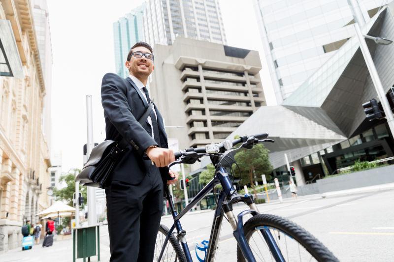 城市建筑背景下推着自行车的年轻商人