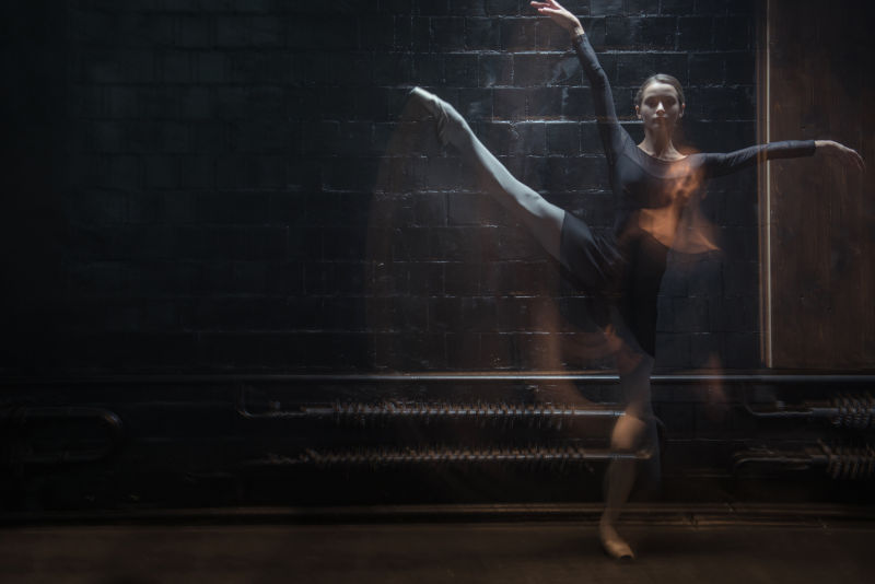 在黑暗的灯光下魅力芭蕾舞演员跳跃的姿势