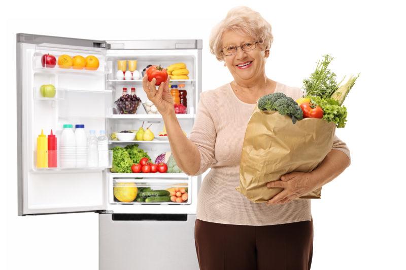 装满食材的冰箱前面有个妇女抱着食材袋子