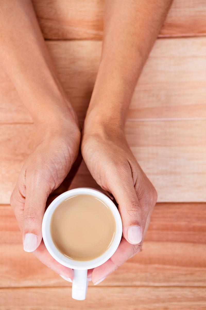 浅色木纹理桌上的一双手抱着咖啡杯