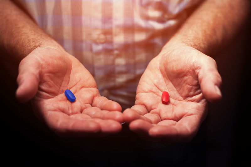 男性手持红色和蓝色药丸