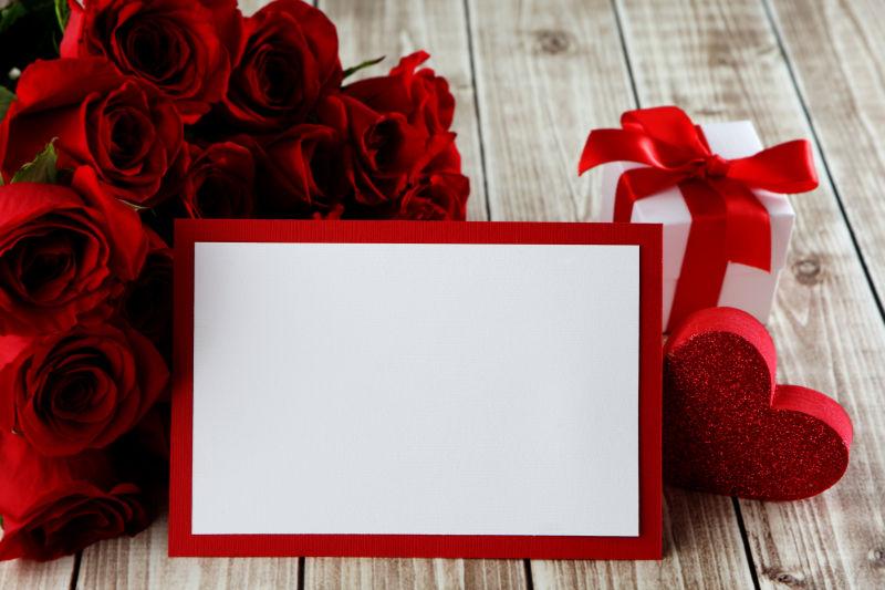 木桌上的玫瑰花束和礼物还有红边白底的卡片