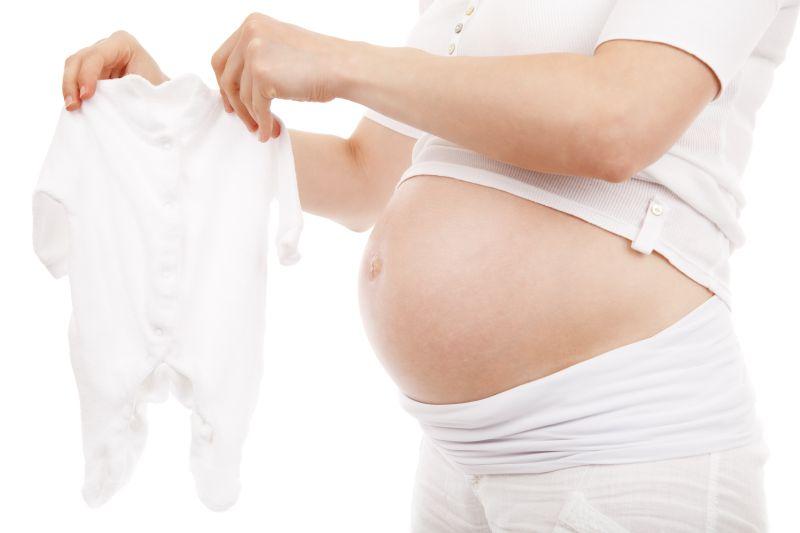 白色背景下拿着小孩衣服的怀孕的孕妇