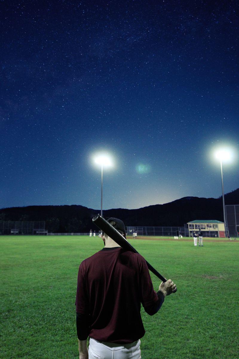 黑夜下在棒球场上拿着棒球棍的男人