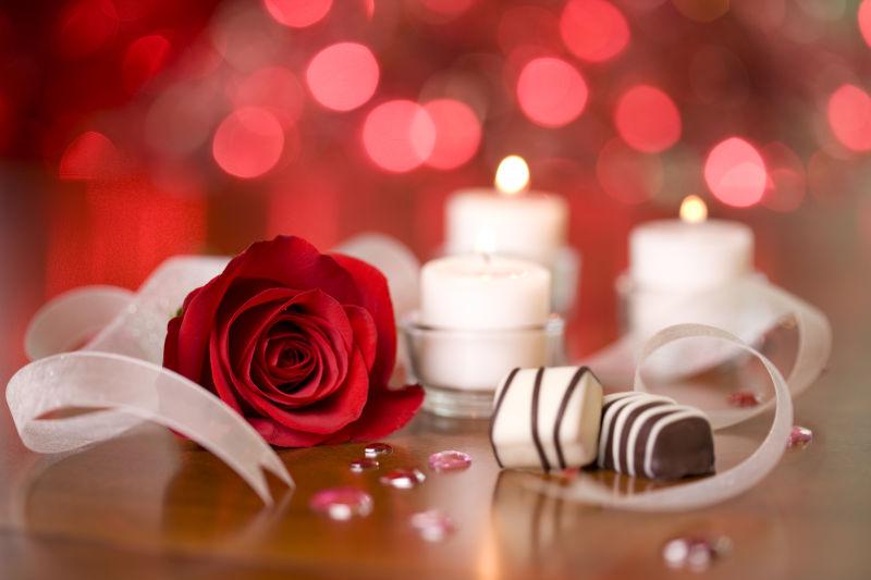 桌子上的红色玫瑰花和巧克力糖还有点燃的白色蜡烛