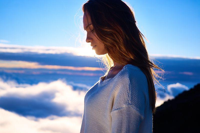 蓝天白云和阳光的背景下的穿着白色针织衫的美女