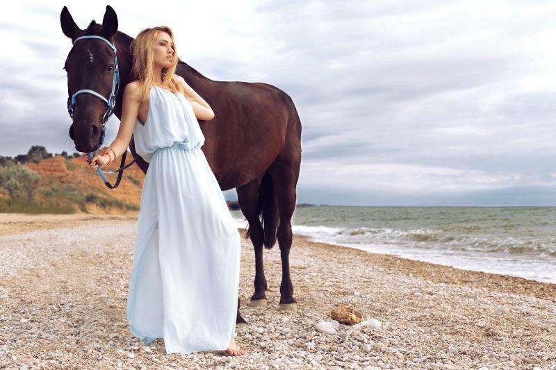 穿着裙子的美女在海边牵着她的马