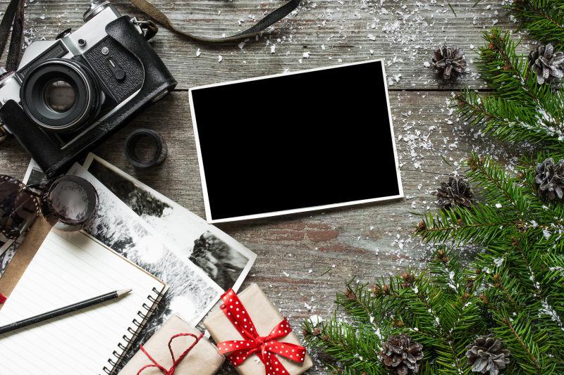 木桌上松树枝旁的礼物盒黑色老式照相机和空白相片