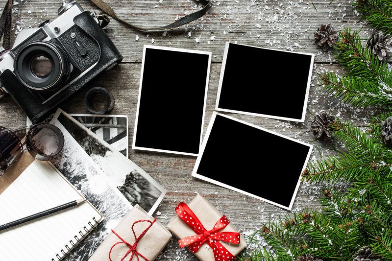 木桌上圣诞树枝旁的礼物盒空白相片和黑色老式照相机