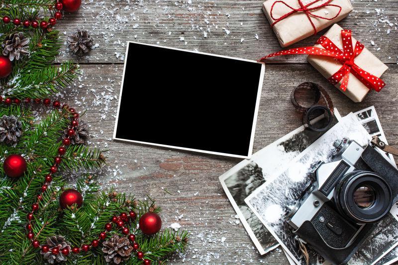 木桌上圣诞树枝旁的礼物盒黑色老式照相机和空白相片