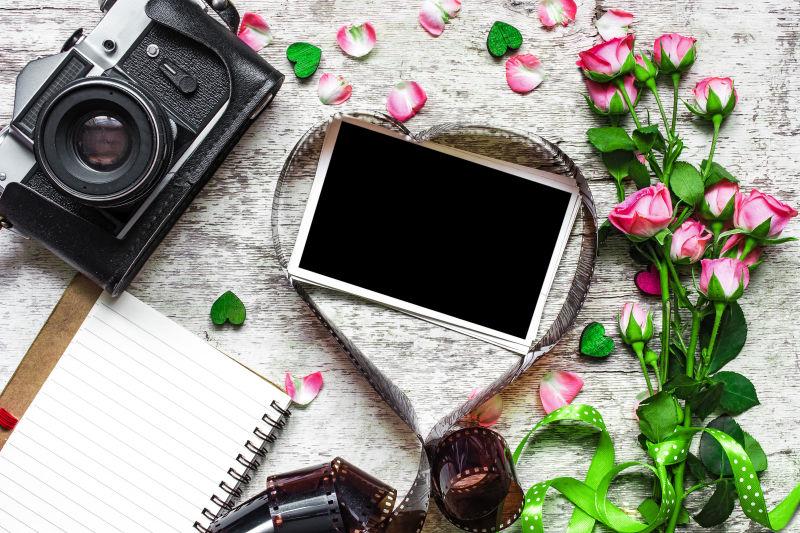 木桌上玫瑰花旁的心形胶卷里的空白相片和黑色复古照相机
