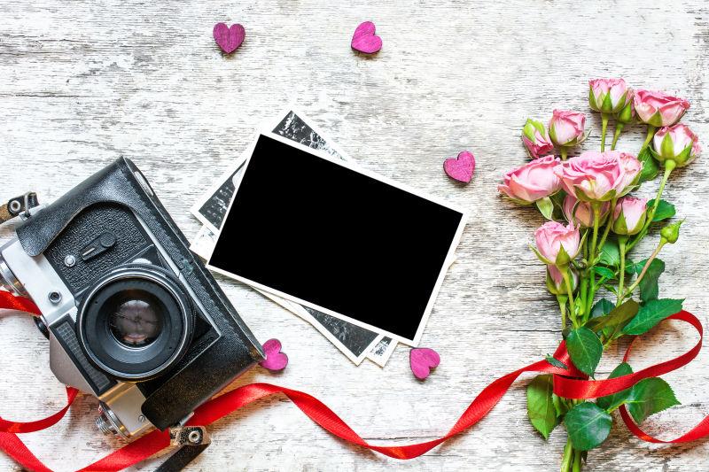 白色桌上一束玫瑰花旁的老式相机和黑色相片