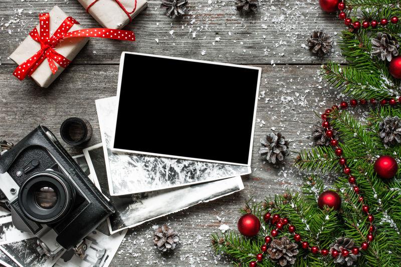 木纹理桌上圣诞树枝旁的复古相机与空白相框