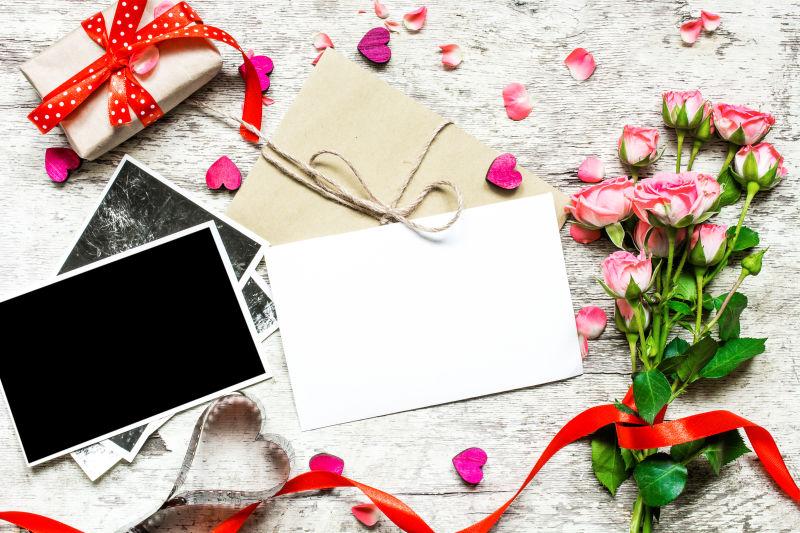 白色桌上玫瑰旁的空白相片和礼物盒
