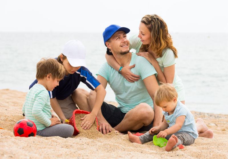 快乐的父母微笑着陪孩子们在海滩上休息