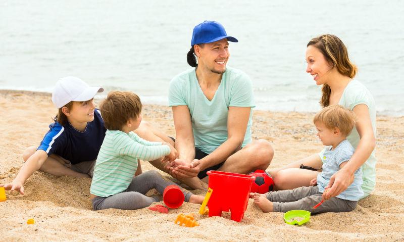 快乐的父母带着三个孩子坐在沙滩