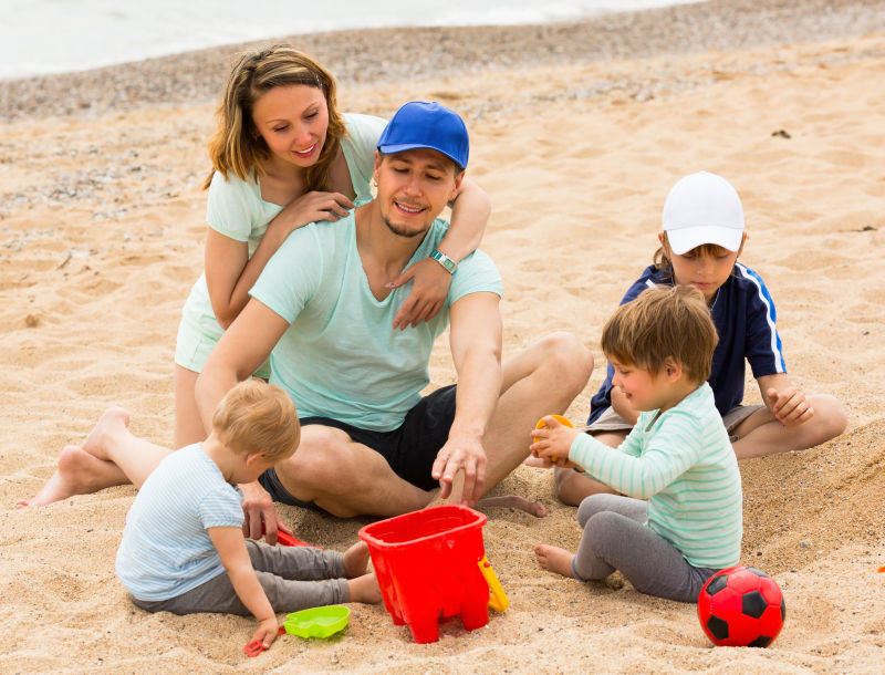 快乐的家庭和三个孩子在海边玩沙子