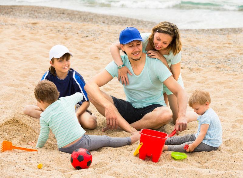 微笑的父母带着三个孩子在沙滩上玩耍
