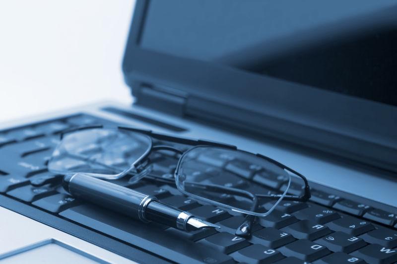 黑色笔记本电脑键盘上的眼镜和钢笔