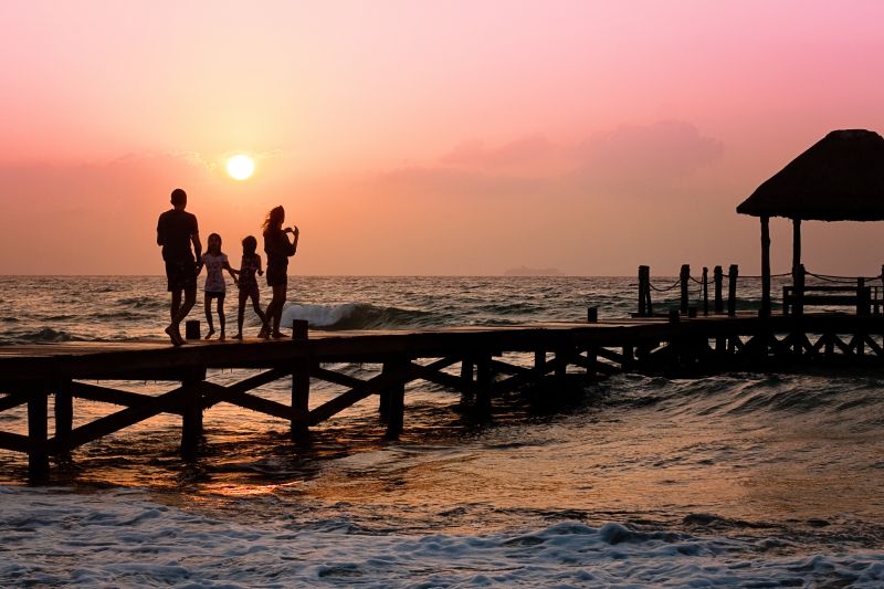 夕阳下在海边木制码头上散步的一家四口