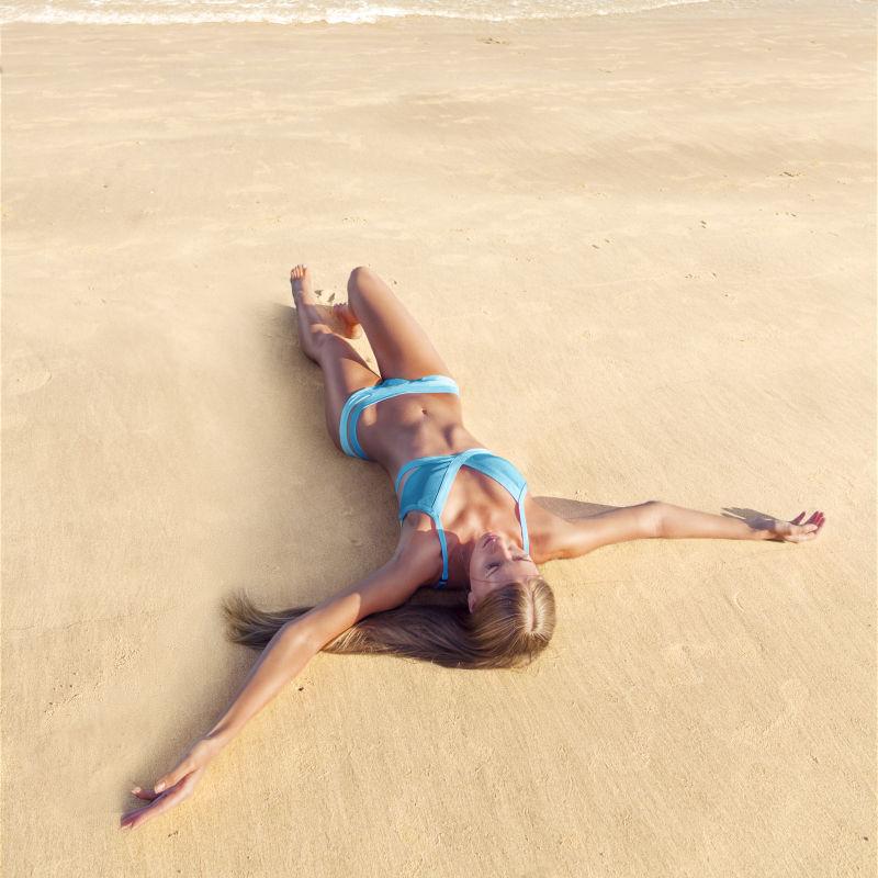 穿着蓝色比基尼躺在沙滩上晒日光浴的美女