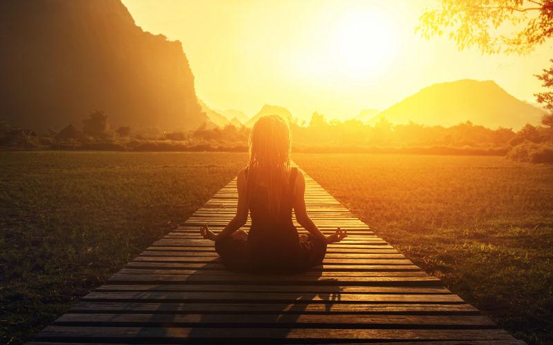 日落下坐在户外瑜伽冥想的女人