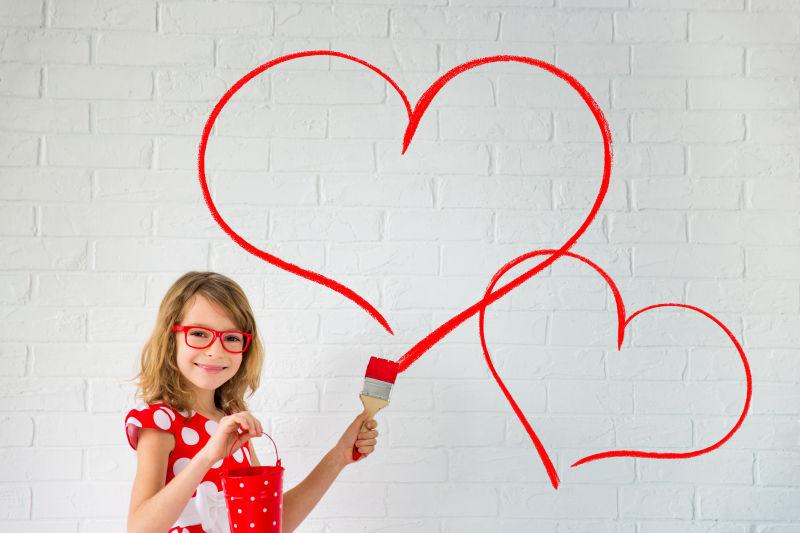 快乐的小女孩在白色墙壁上画出两颗红心