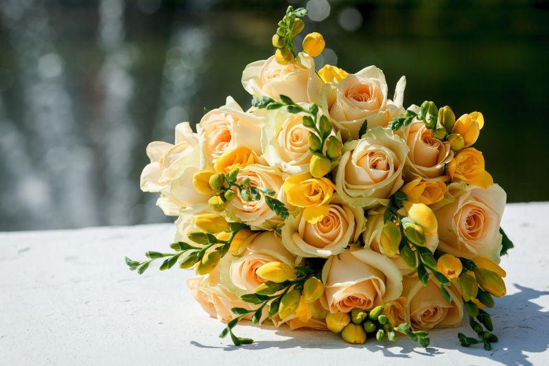 阳光下放在白色桌上的黄色的新娘手捧花