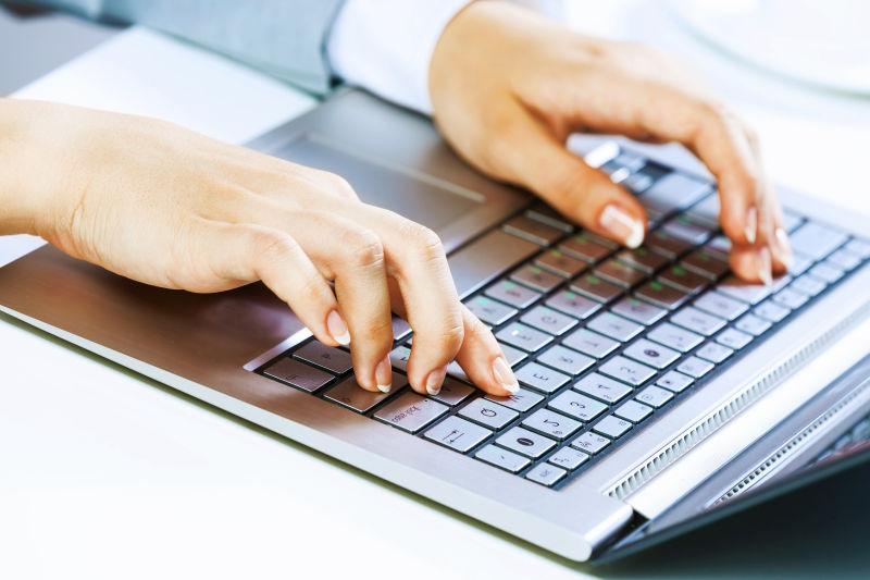 白色桌上在笔记本电脑键盘上打字的女人的手