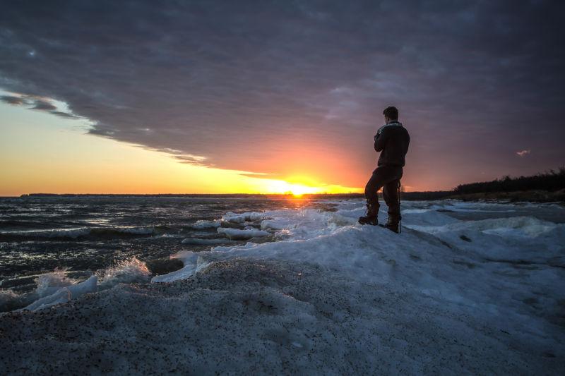 冬季日落背景下男摄影师站在冰封的湖面上
