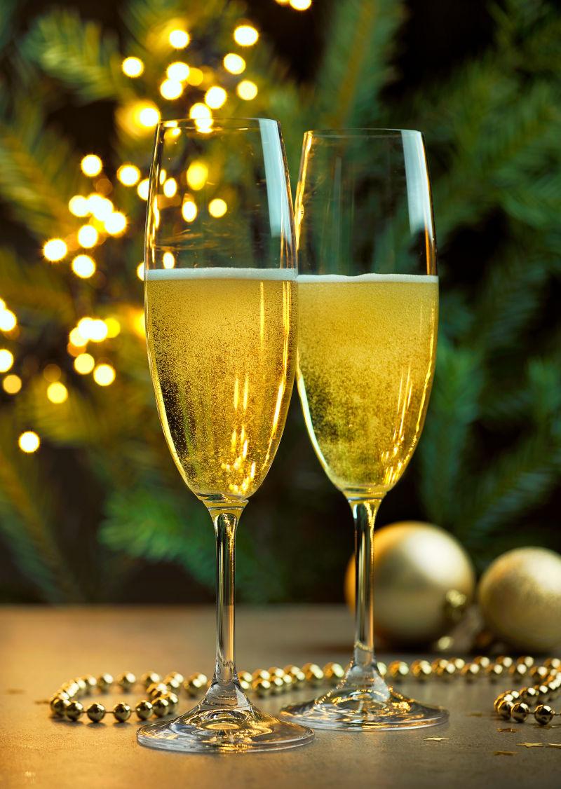 绿色树枝上的金色小彩灯背景下的两杯香槟酒