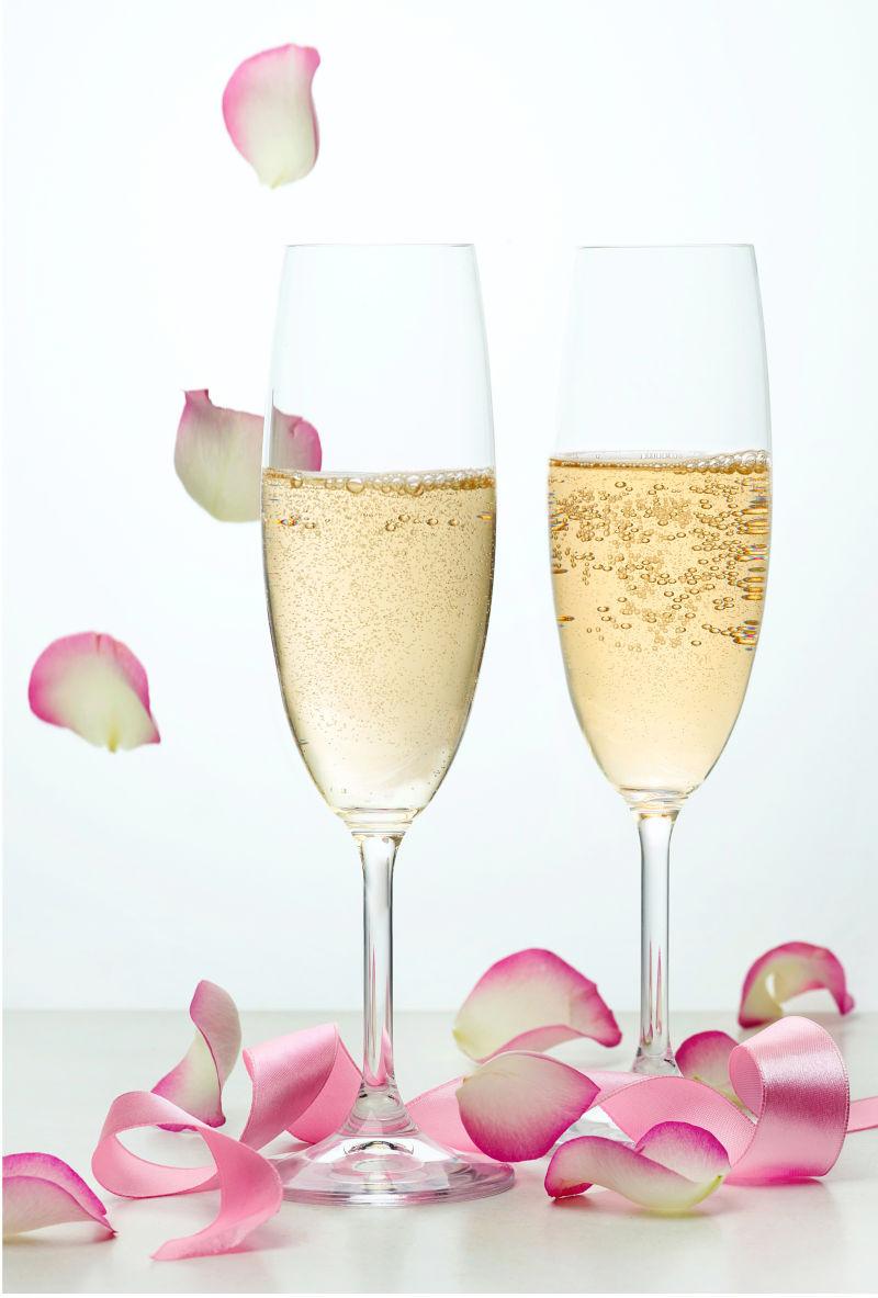 白色背景上的两杯香槟酒和散落的粉红色花瓣