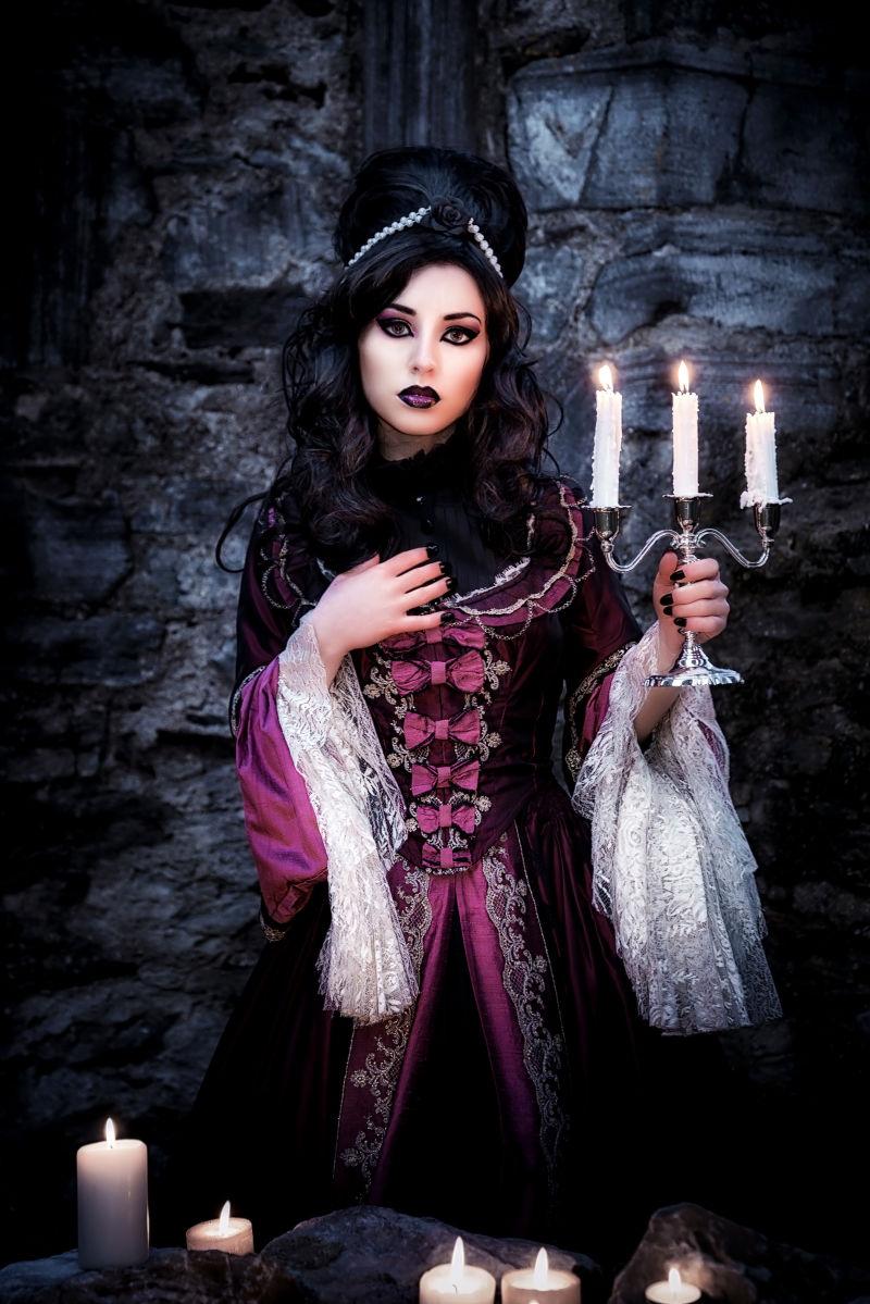 黑色神秘背景中拿着蜡烛的哥特女孩