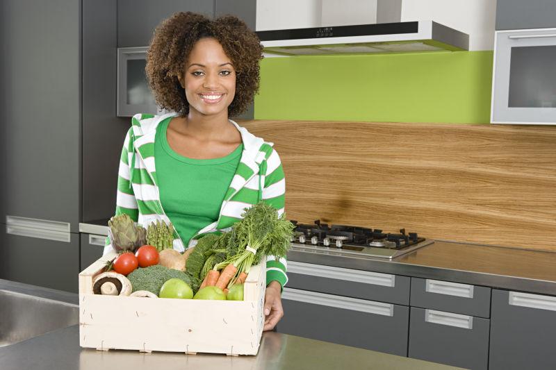 厨房里黑人妇女端着装满蔬菜的箱子