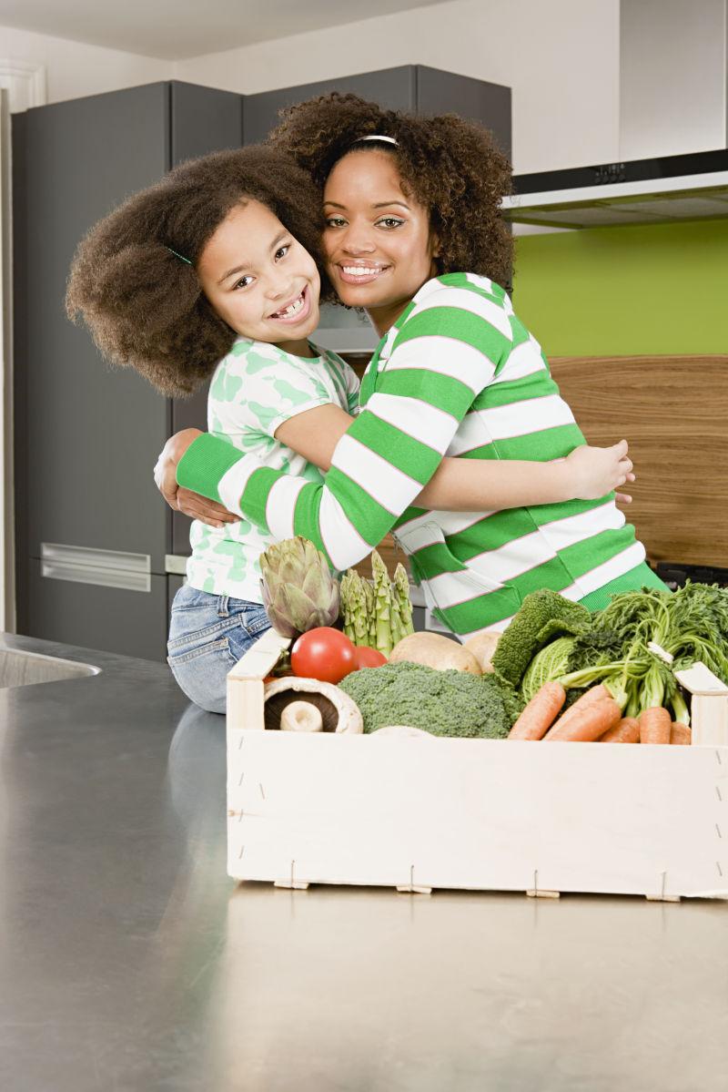 装满蔬菜的箱子后面两个抱在一起的母女