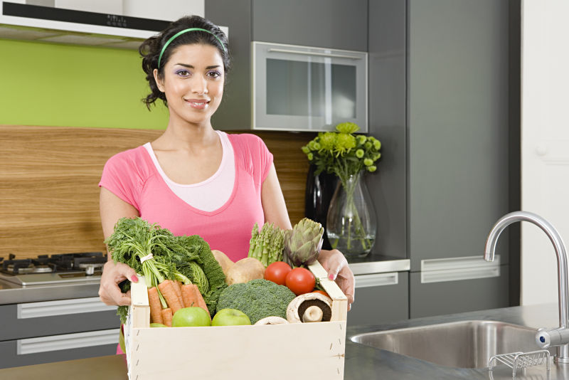 厨房里妇女抱着装满绿色蔬菜的箱子
