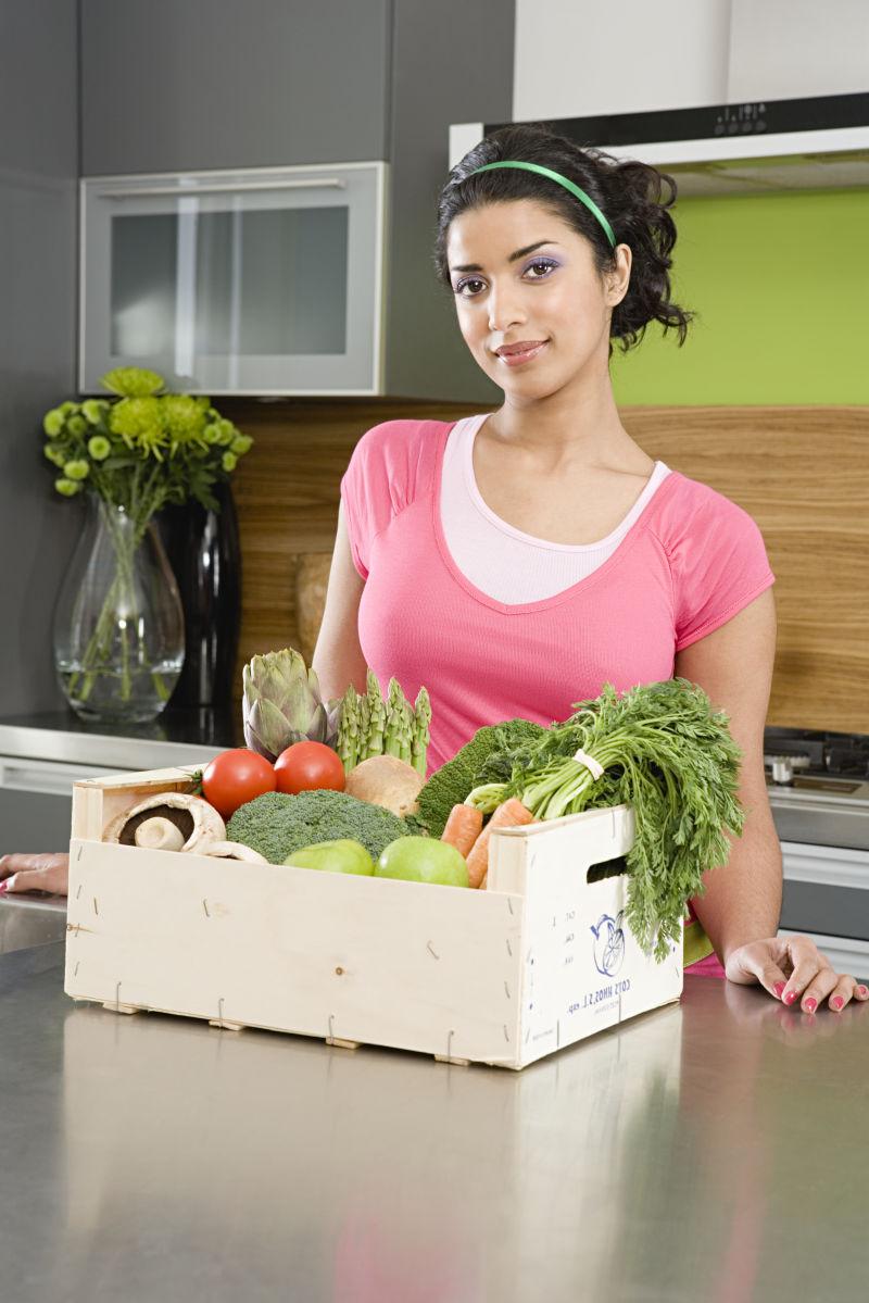 厨房里的年轻妇女前面放着装满蔬菜的箱子